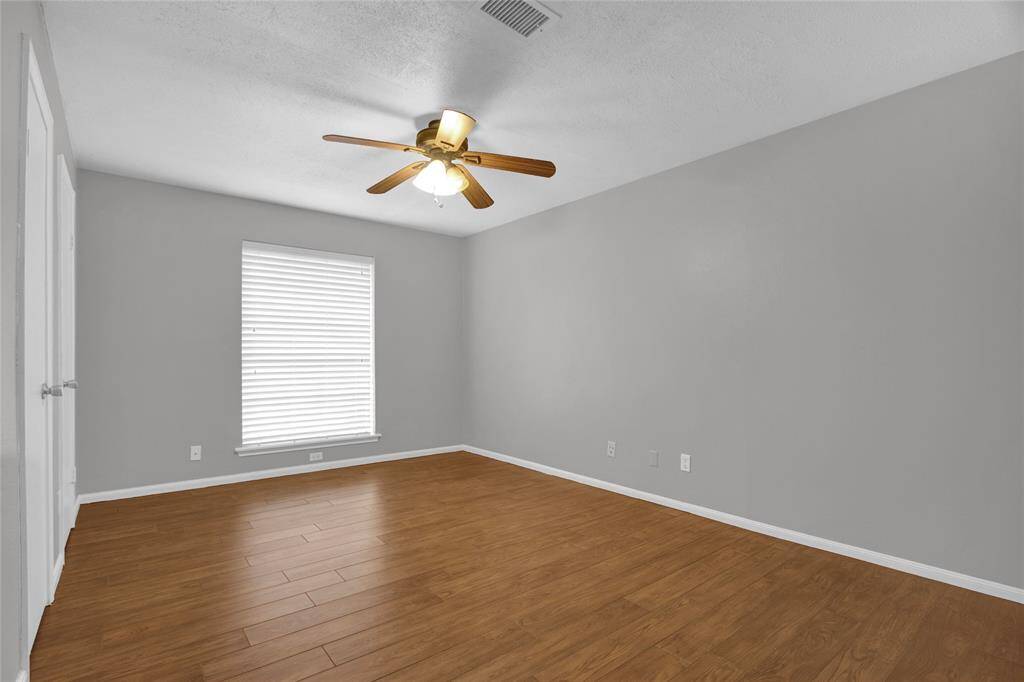 Spacious primary suite with elegant hardwood look tile floors and a refreshing ceiling fan, bathed in natural light from a large window.