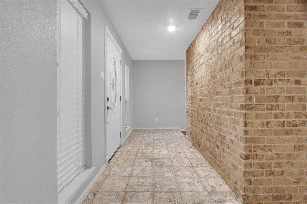 Welcome into this inviting foyer, featuring elegant tile flooring and a warm brick accent wall, creating a perfect first impression of your new home.