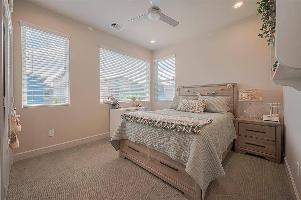 Wake up to sunshine in this light-filled bedroom featuring corner windows, plush carpet, a modern ceiling fan, and serene neutral tones—an inviting space for rest or creativity.