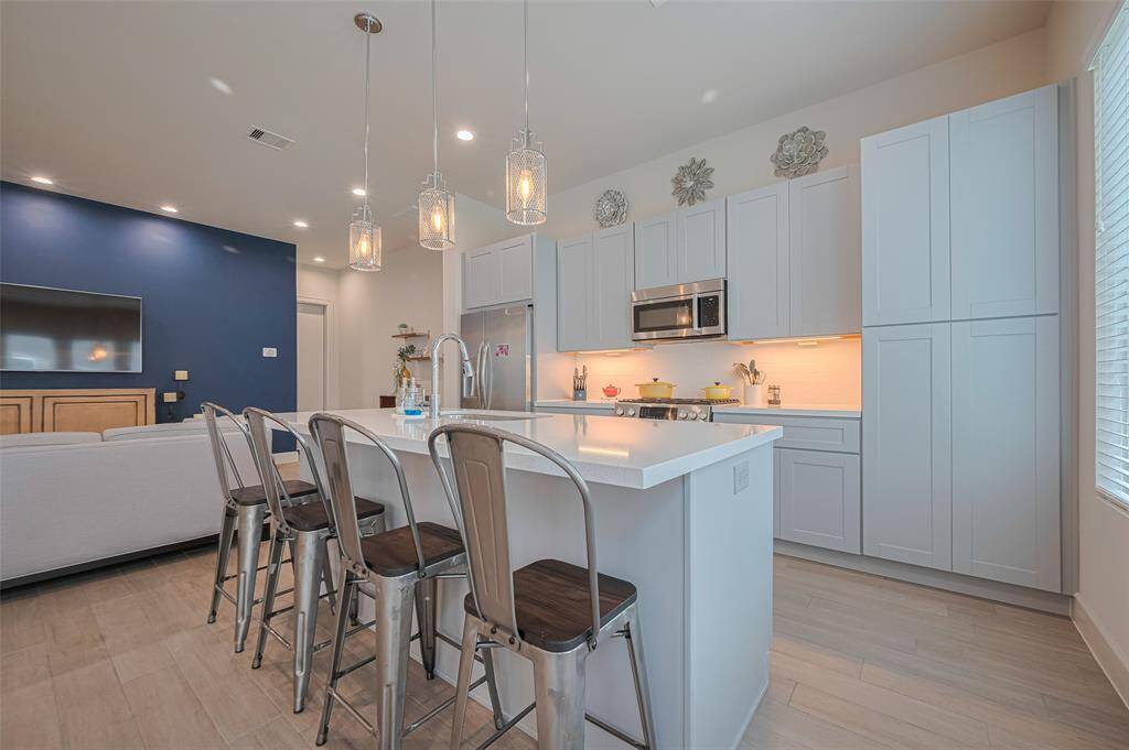 Sleek and functional kitchen featuring quartz countertops, a large center island with seating, stainless steel appliances, and modern pendant lighting—crafted for both cooking and connection.