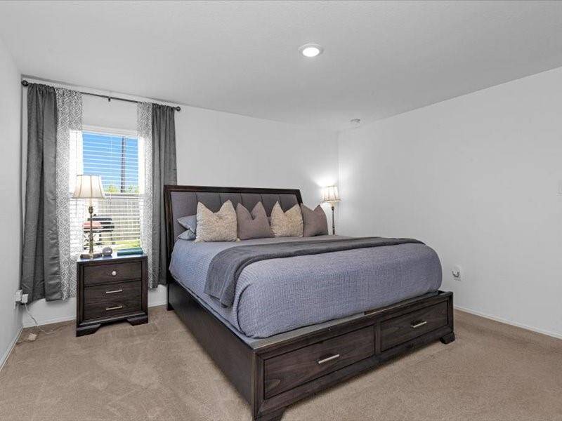 The spacious primary bedroom offers a serene atmosphere, with a large window that fills the room with light and soft, luxurious carpeting underfoot.