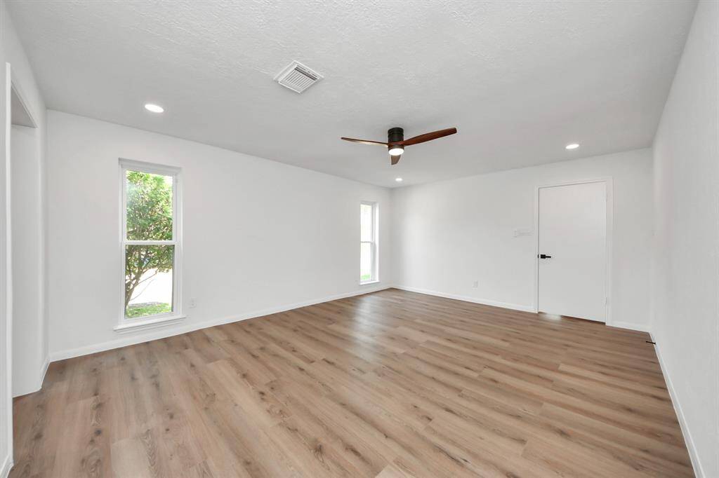 The spacious primary bedroom offers a peaceful retreat with sleek wood-look flooring, recessed lighting, and large windows that flood the room with natural light.