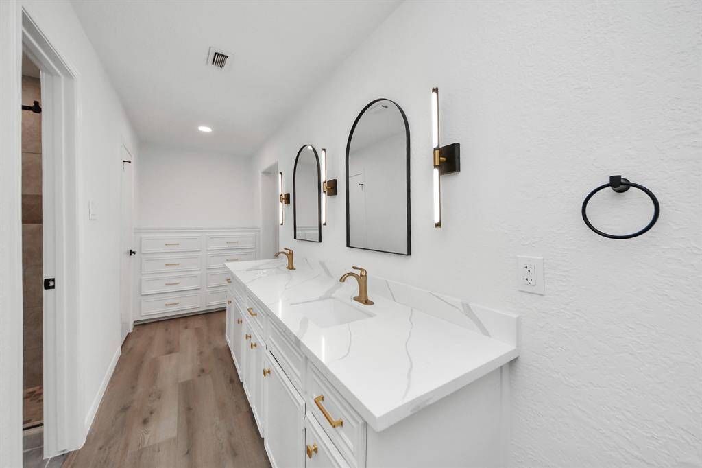 The stylish primary bathroom features a double vanity with quartz countertops, matte gold fixtures, and designer lighting flanking elegant arched mirrors.