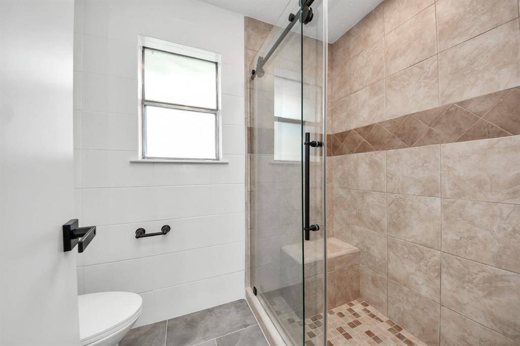 The primary bathroom features a spacious walk-in shower with floor-to-ceiling tile, a built-in bench, and sleek frameless glass doors.