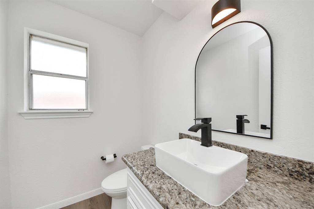This stylish half bath features a modern vessel sink atop granite counters, paired with matte black fixtures and a bold arched mirror—delivering a sleek, contemporary feel perfect for guests.