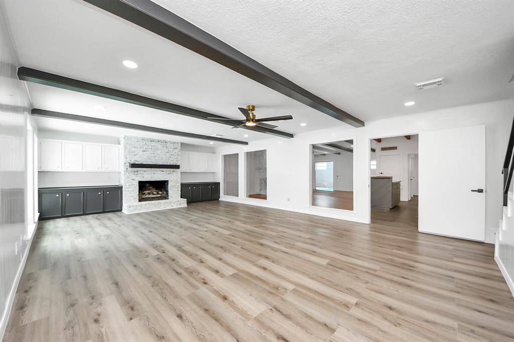 The expansive family room is a true showstopper, featuring exposed ceiling beams, a modern ceiling fan, and a whitewashed brick fireplace flanked by built-in cabinetry.