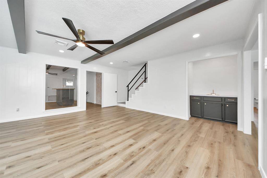The oversized family room impresses with dramatic ceiling beams, wide-plank flooring, and expansive windows overlooking the pool. A built-in wet bar and striking black accents make this space both stylish and functional for entertaining.