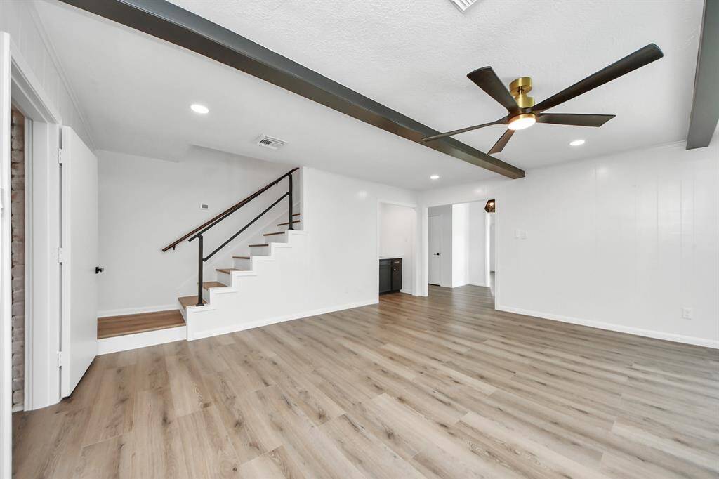 A modern staircase with sleek black railing anchors the family room, complementing the rich ceiling beams and contemporary ceiling fan.