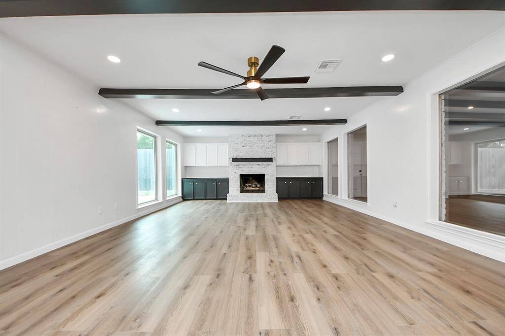 Framed by oversized windows and rich wood flooring, this inviting family room features a stunning whitewashed fireplace, exposed ceiling beams, and custom built-ins.