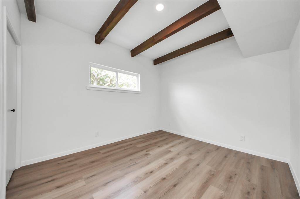 This secondary bedroom combines charm and character with its exposed wood beams, vaulted ceiling, and rich flooring.