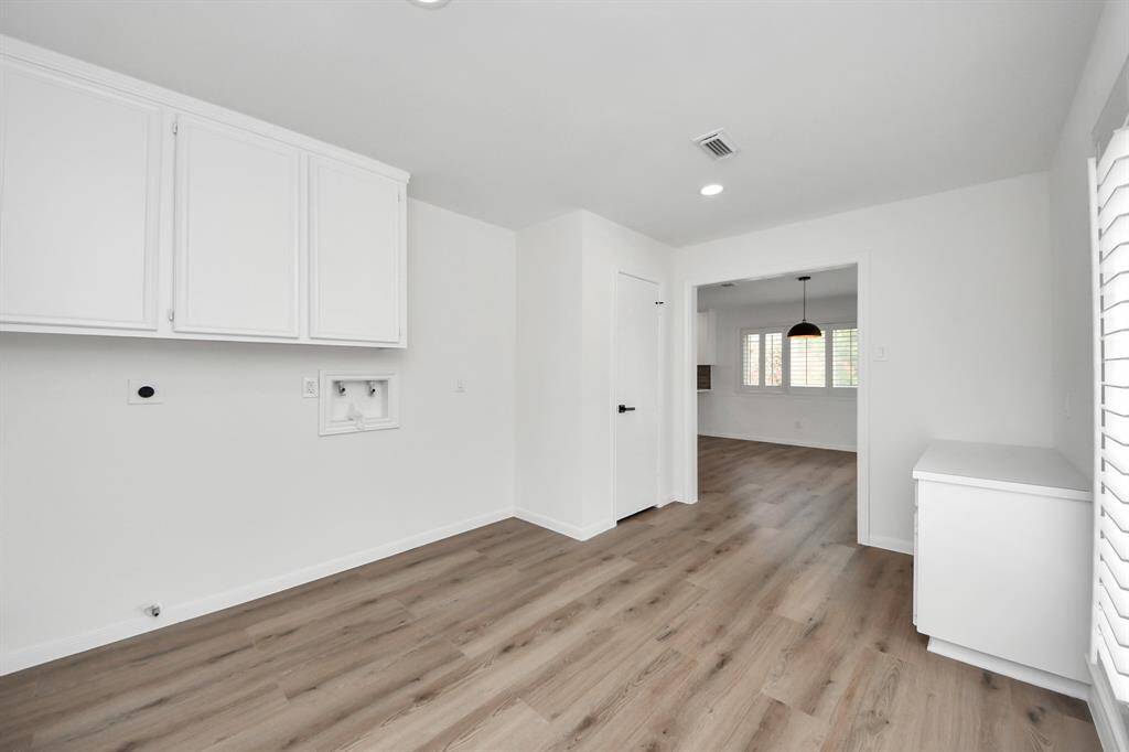 This spacious laundry room offers abundant storage with upper cabinetry and a built-in workstation, all set against stylish wide-plank flooring and fresh white finishes.