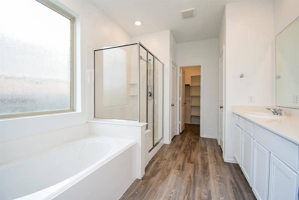 Experience luxury in this en-suite bathroom featuring a stylish vanity, a relaxing soaking tub by the window, a spacious walk-in shower, and an oversized walk-in closet.