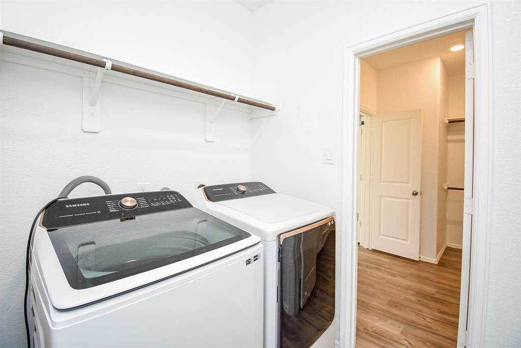 Convenient laundry room connects entrance to primary bathroom with modern appliances and ample shelving, perfect for streamlined chores.