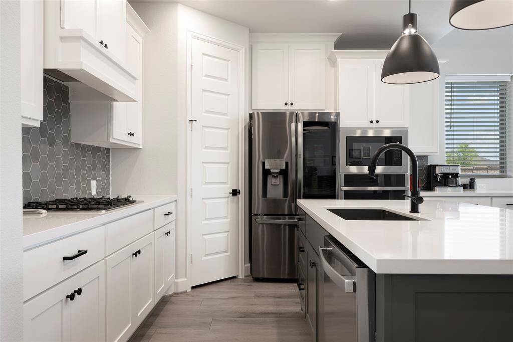 Modern kitchen with sleek stainless steel appliances, white cabinetry, and a stylish hexagonal tile backsplash. Features a spacious island with a black faucet and pendant lighting, creating a bright and inviting space.