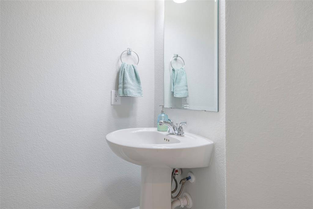 This photo shows a compact, modern half-bathroom featuring a pedestal sink with a mirror above, a towel ring for a hand towel, and a clean, minimalist design.