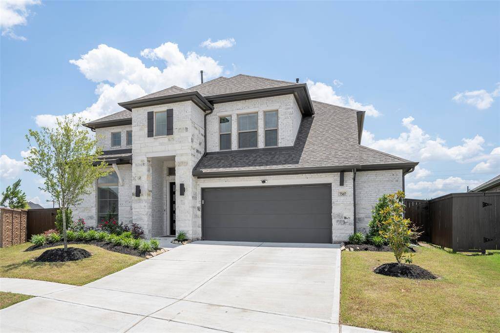 This beautiful two-story home features a modern brick exterior with a dark shingled roof. It has a spacious two-car garage, a neatly landscaped front yard with trees and shrubs, and is situated on a quiet street.
