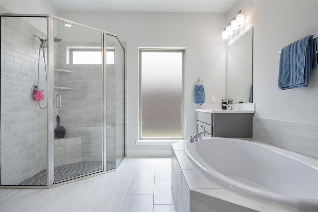 This modern bathroom features a spacious walk-in shower with glass doors, a large soaking tub, and a sleek vanity with ample lighting. The frosted window provides natural light while maintaining privacy, complementing the clean, contemporary design.