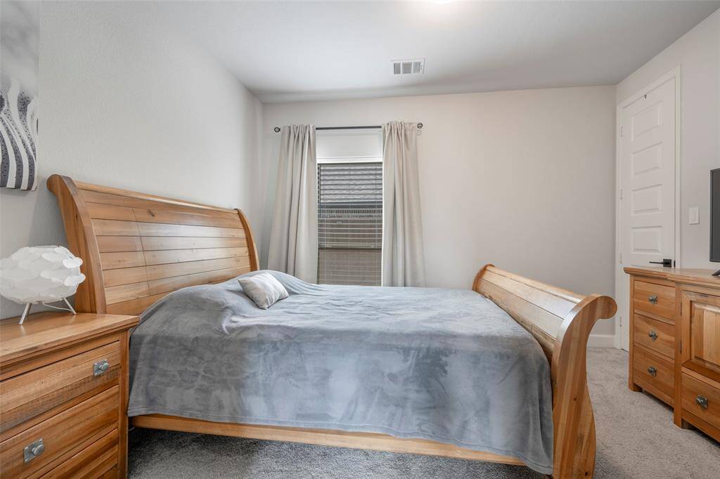 This cozy bedroom features a wooden sleigh bed, matching nightstands, and a dresser. The room is carpeted, with neutral walls and a window that lets in natural light, creating a warm and inviting atmosphere.
