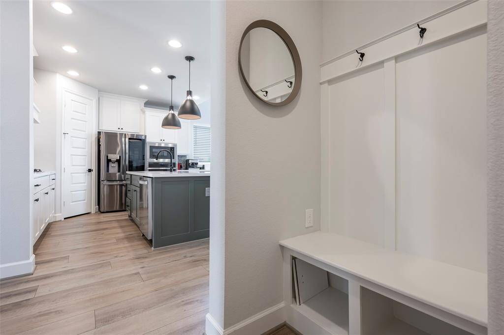 A functional mudroom area featuring a bench, hooks. The space is bright and airy with light wood flooring.