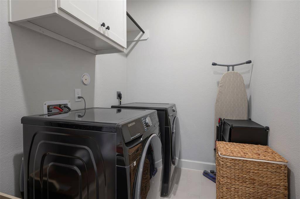 This photo shows a well-organized laundry room featuring modern appliances, overhead storage cabinets. The space is clean with neutral colors, offering a functional area for laundry tasks.