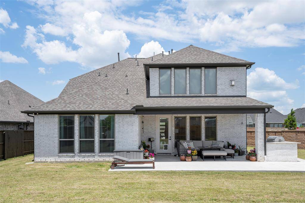 This photo features a modern two-story home with a light brick exterior and a spacious backyard. .