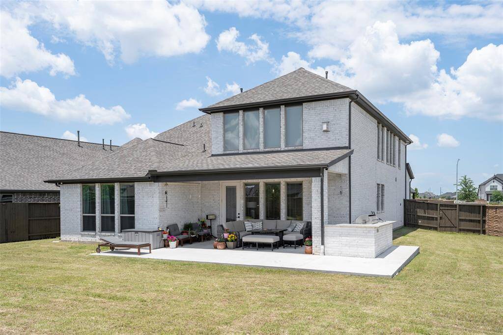 This modern two-story home features a spacious backyard with a large patio, perfect for outdoor entertaining. The exterior is a stylish light brick with ample windows allowing natural light to flood inside.