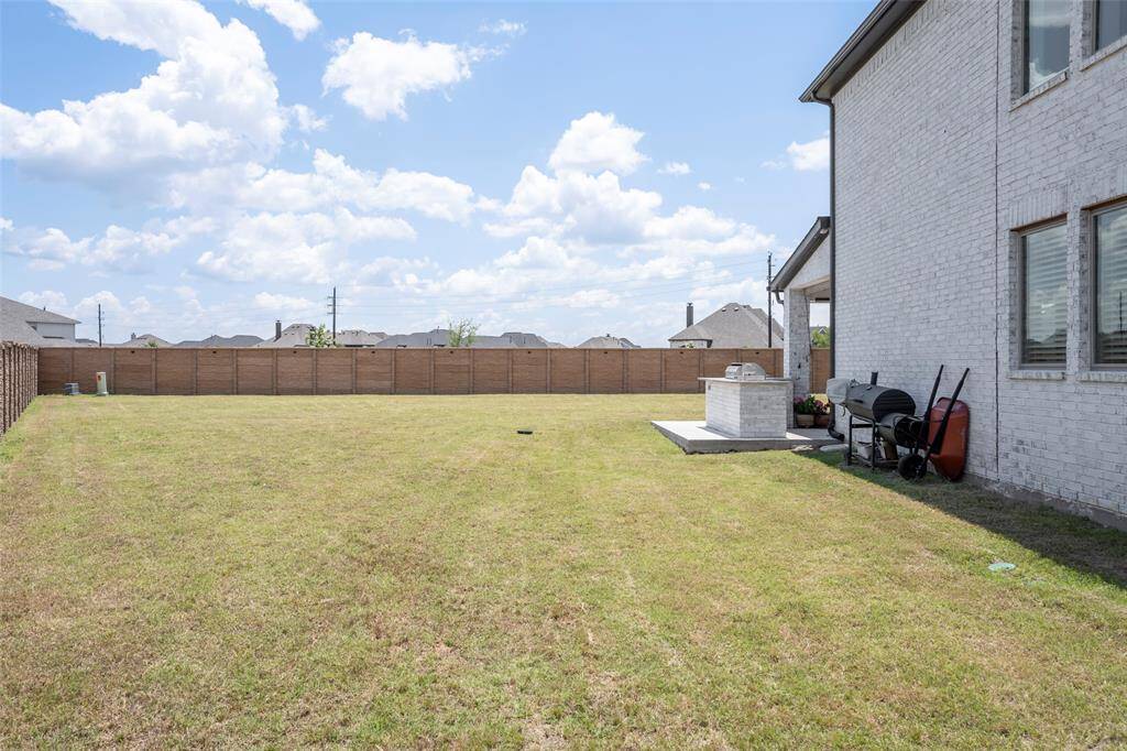 Spacious backyard with a large grassy area, perfect for outdoor activities. Features a patio area with a grill and a brick fence for privacy. Ideal for entertaining and enjoying sunny days.