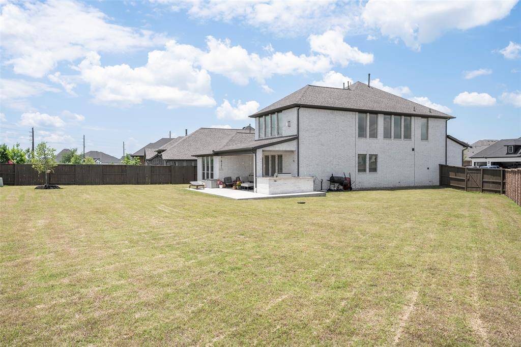 This photo shows the back of a spacious two-story house with a large, well-maintained backyard. The home features a patio area and is surrounded by a wooden fence, offering privacy and ample outdoor space.