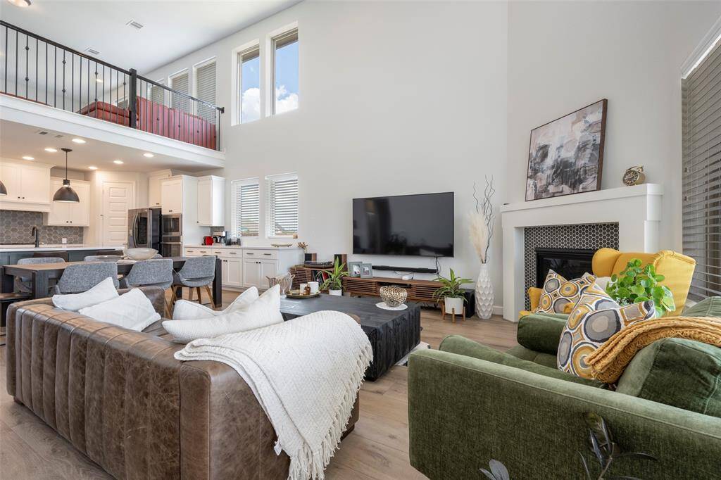 Spacious living room with high ceilings and abundant natural light. Features include a modern open-concept kitchen, cozy fireplace, stylish furnishings, and a loft area. Perfect for comfortable living and entertaining.