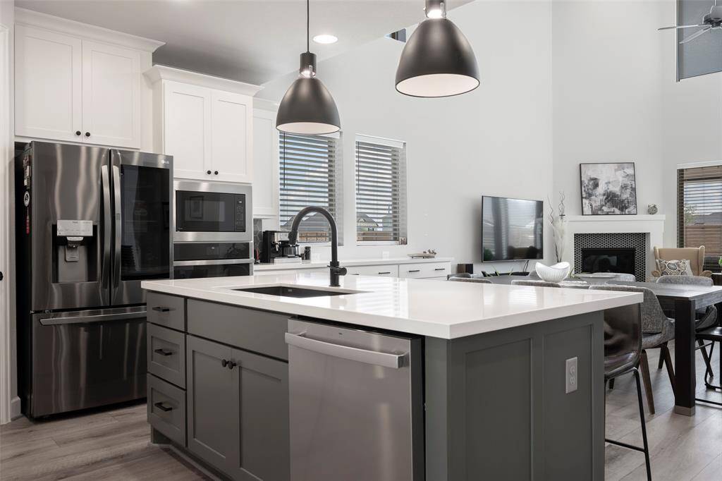 Modern open-concept kitchen and living area featuring sleek stainless steel appliances, a spacious island with a sink, and ample cabinetry. The living space includes a cozy fireplace and large windows for natural light.