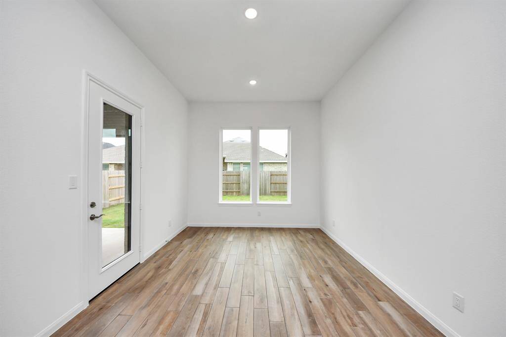 Bright and inviting, this room features wood flooring, two large windows for abundant natural light, and a glass door opening to a fenced backyard—ideal for a cozy dining or living area.