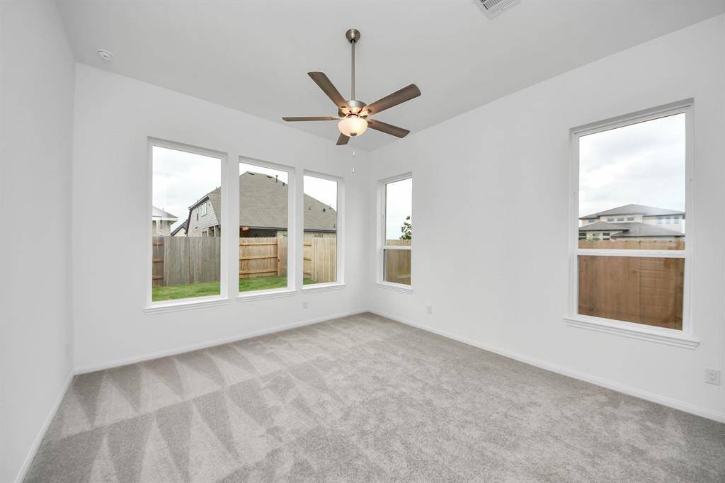 Bright room with large windows, abundant natural light, neutral carpet, and a ceiling fan, overlooking a fenced backyard.