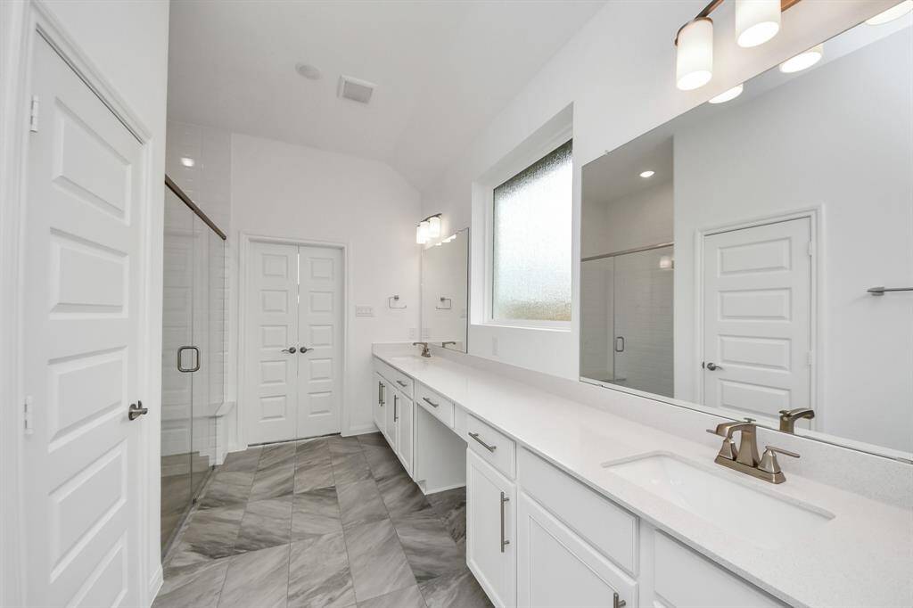 Experience luxury in this modern bathroom with a spacious double vanity, sleek white cabinetry, and a large mirror. Enjoy a walk-in glass shower, stylish tile flooring, and ample natural light from a frosted window, creating a bright and inviting space.