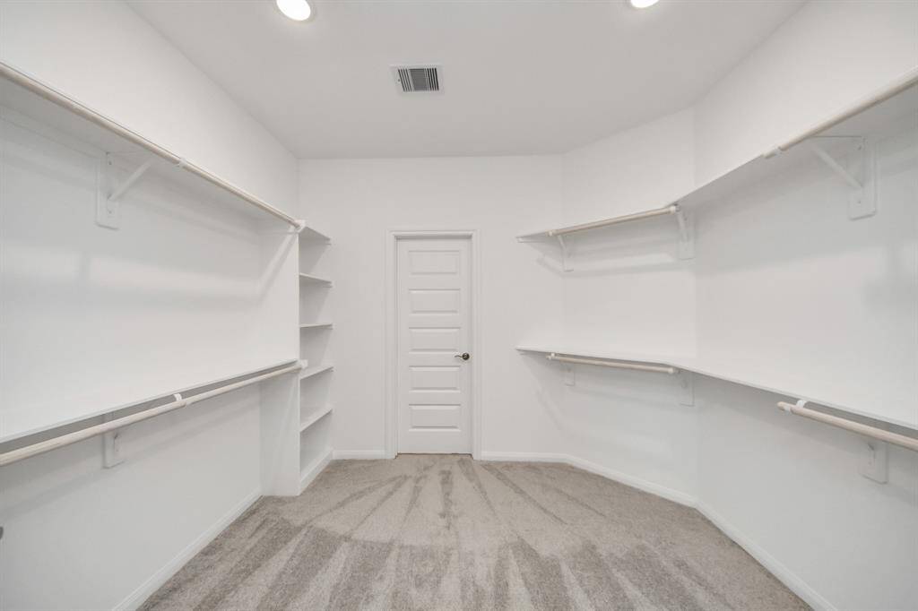 Spacious walk-in closet with ample shelves, hanging rods, bright lighting, and neutral carpet—ideal for organized storage.