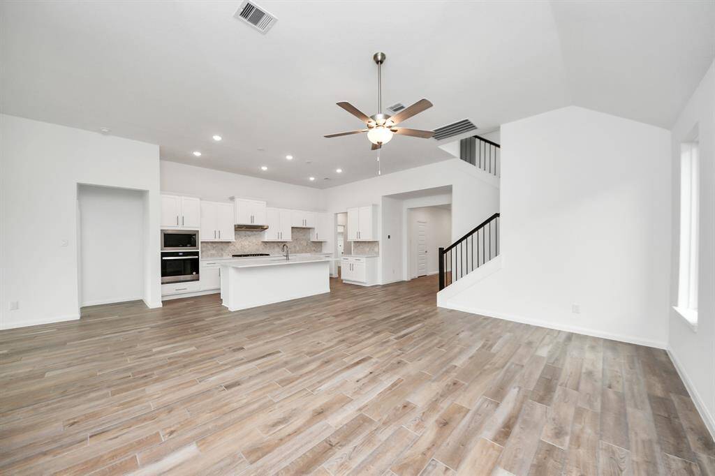 Experience the elegance of this open-concept living area with hardwood floors, high ceilings, and abundant natural light. The modern kitchen features sleek white cabinetry, a large island, and built-in appliances, perfect for entertaining.