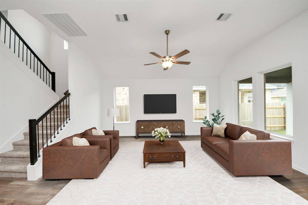 VIRTUAL IMAGE!Experience a bright, spacious living room with large windows and modern features. Enjoy two cozy brown sofas, a central coffee table, and a sleek wall-mounted TV. A stylish staircase with contemporary railing leads to the upper level, enhancing the room's open feel.