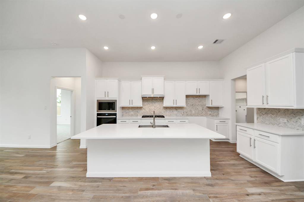 Experience the elegance of this kitchen with its open layout, sleek white cabinetry, and large central island with a sink. Enjoy built-in appliances, a stylish backsplash, and the warm ambiance created by recessed lighting and wood-style flooring.