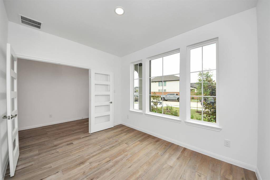 Bright and inviting room with large windows, wood-look flooring, and modern white walls. Features stylish double doors, perfect for a home office or sitting area.