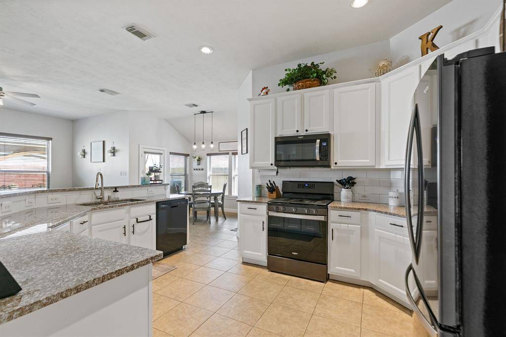 This photo reveals how open this kitchen really is. It's open to a bright dining area with large windows and a tiled floor, creating a spacious and inviting atmosphere.