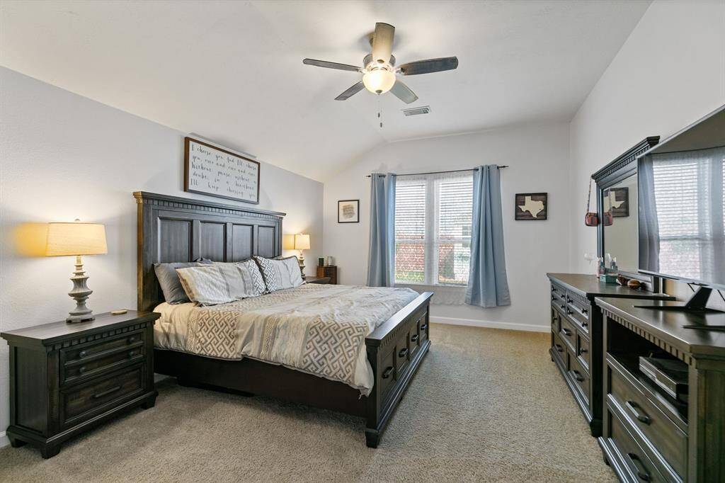 This spacious bedroom features a vaulted ceiling, soft carpet, and ample natural light from the large windows.  Complemented by a ceiling fan for comfort, this primary room is great for relaxation.