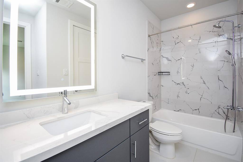 This room is complete with a shower tub/combo, tile floors, quartz countertops, and a large mirror.