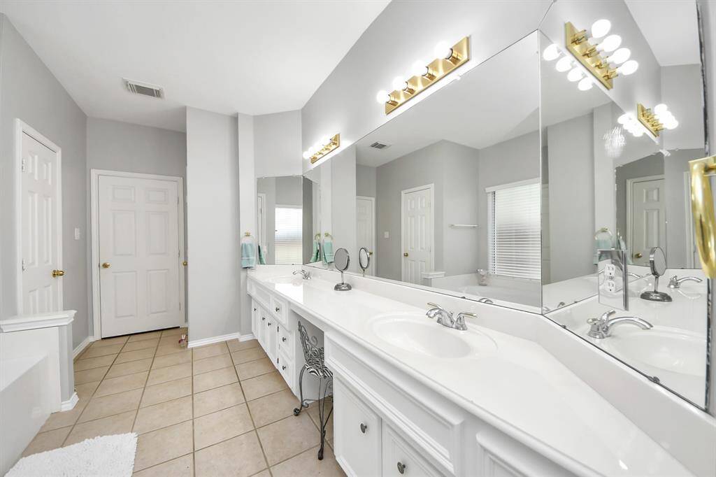 Above the vanity, a large frameless glass mirror reflects the light, while vanity lighting overhead casts a soft, welcoming glow throughout the space.