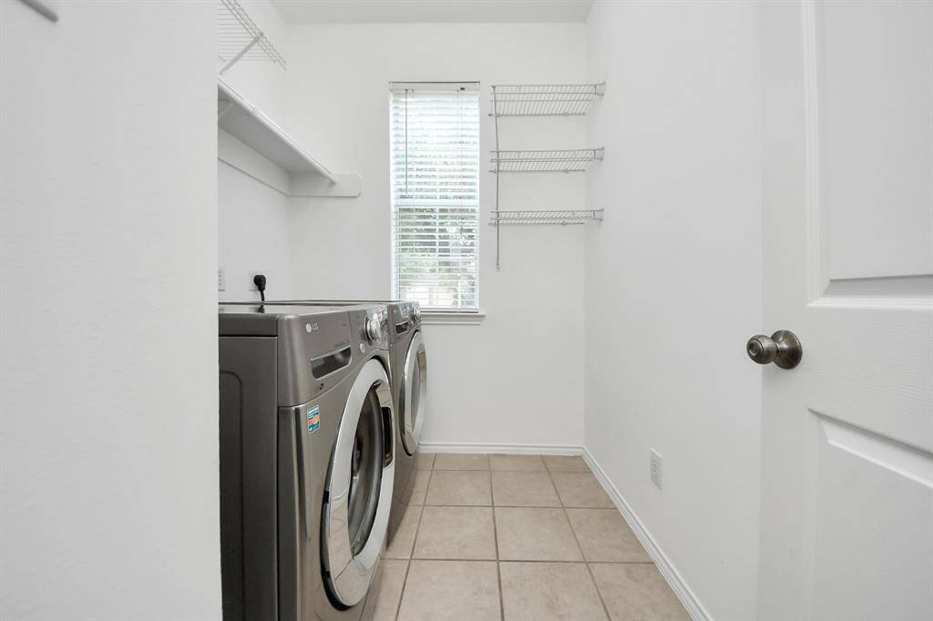 The laundry room features tile flooring, ensuring easy maintenance and durability. A window allows for natural light to brighten the space, creating a more pleasant environment. Shelving provides convenient storage for laundry essentials, keeping everything organized and within reach.