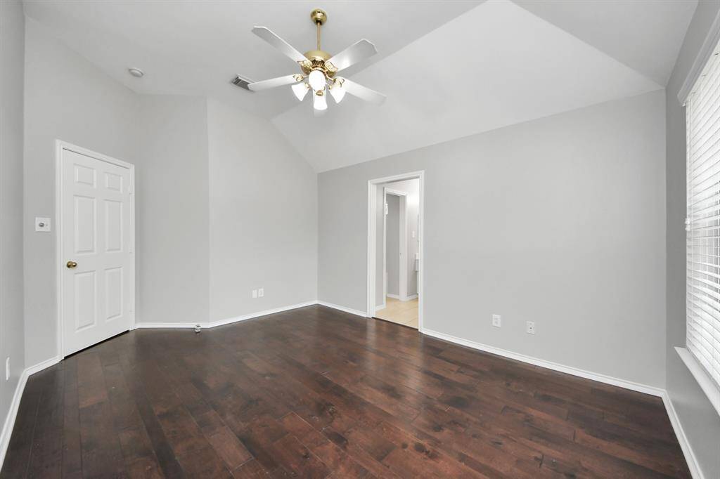 The vaulted ceiling, paired with a ceiling fan, adds to the room's sense of openness and comfort. The gleaming wood floors bring an elegant touch, complementing the room’s modern and timeless appeal.