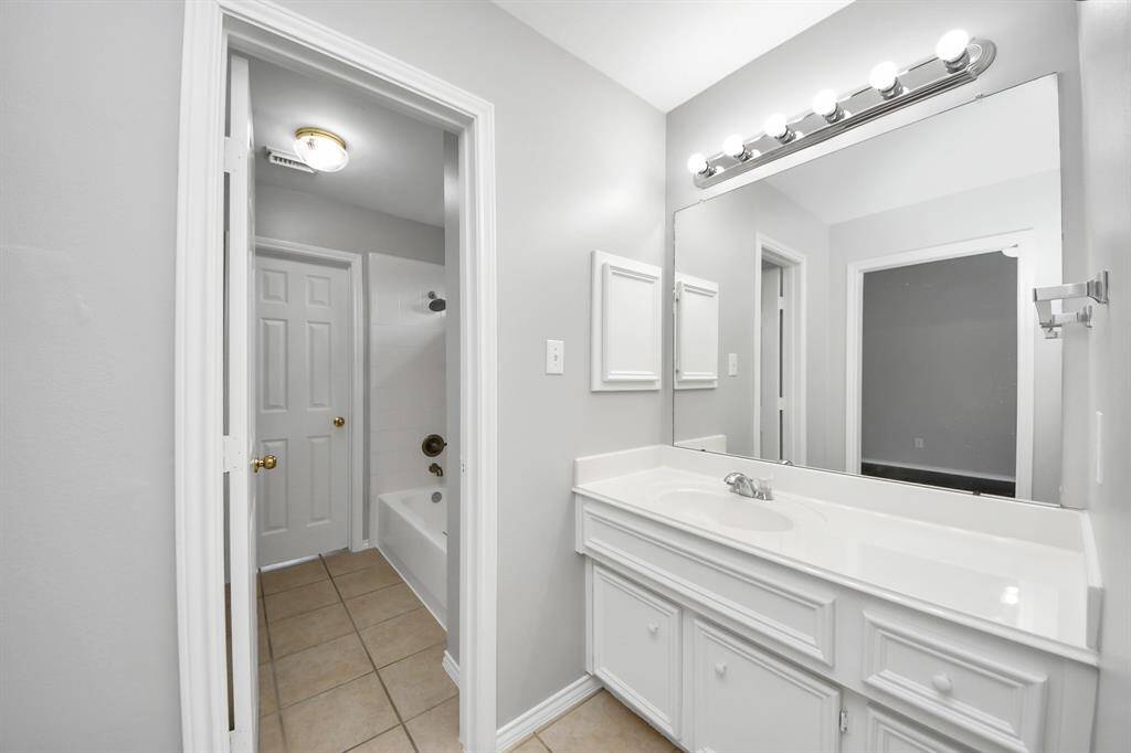 This Jack and Jill bathroom is designed for convenience and privacy, featuring two separate sink vanities, each with crisp white cabinetry and large frameless mirrors. Overhead vanity lighting provides ample illumination for each vanity.