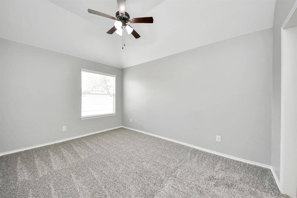 The final secondary bedroom offers plush carpet that adds warmth and comfort. The high vaulted ceiling, paired with a ceiling fan, enhances the sense of spaciousness and ensures optimal airflow. A large window floods the room with natural light, creating a bright and airy space perfect for rest or relaxation.