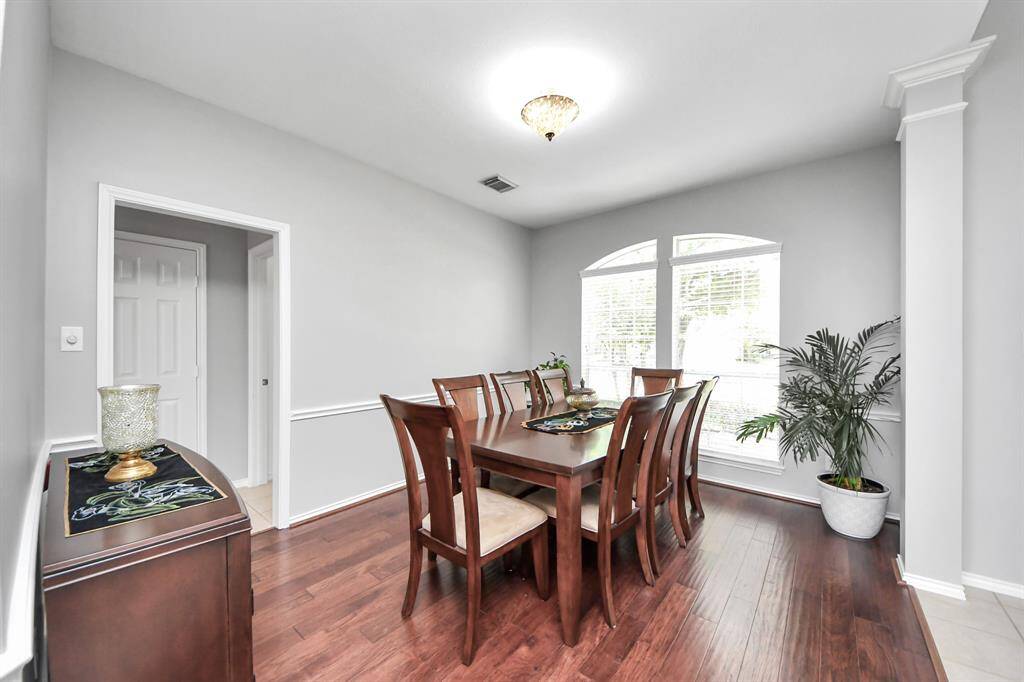 The oversized formal dining room features elegant chair-rail molding, gleaming wood floors, a high ceiling, and large windows that flood the space with natural light, creating a bright and welcoming atmosphere.