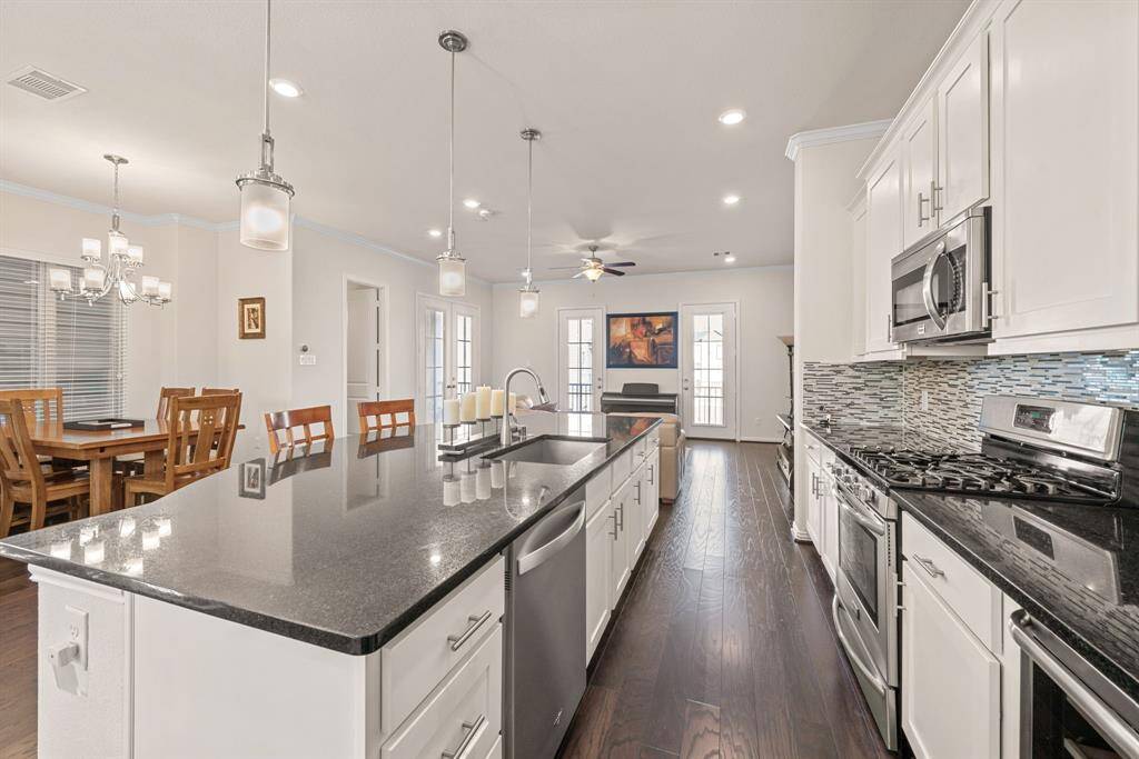 This dining area features a wooden table with six chairs, set against a backdrop of light walls and hardwood floors. A modern chandelier hangs overhead, and large windows provide ample natural light. A staircase with decorative railing is visible on the side.