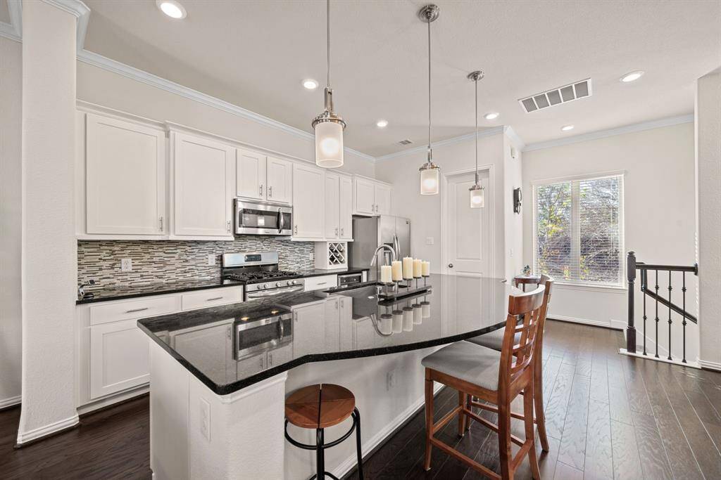This photo showcases a dining area with a wooden table and chairs, elegant chandelier, and large window with blinds. The space is adjacent to a staircase with wrought iron railings, adding a touch of sophistication.