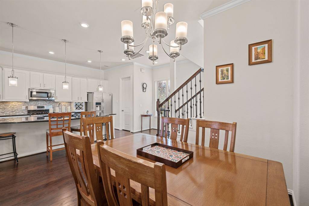 This photo showcases an open-concept living space featuring a dining area with a wooden table, a modern kitchen with a large island and bar seating, and a cozy living room. The room is well-lit with pendant and ceiling lights, and the hardwood floors add warmth.